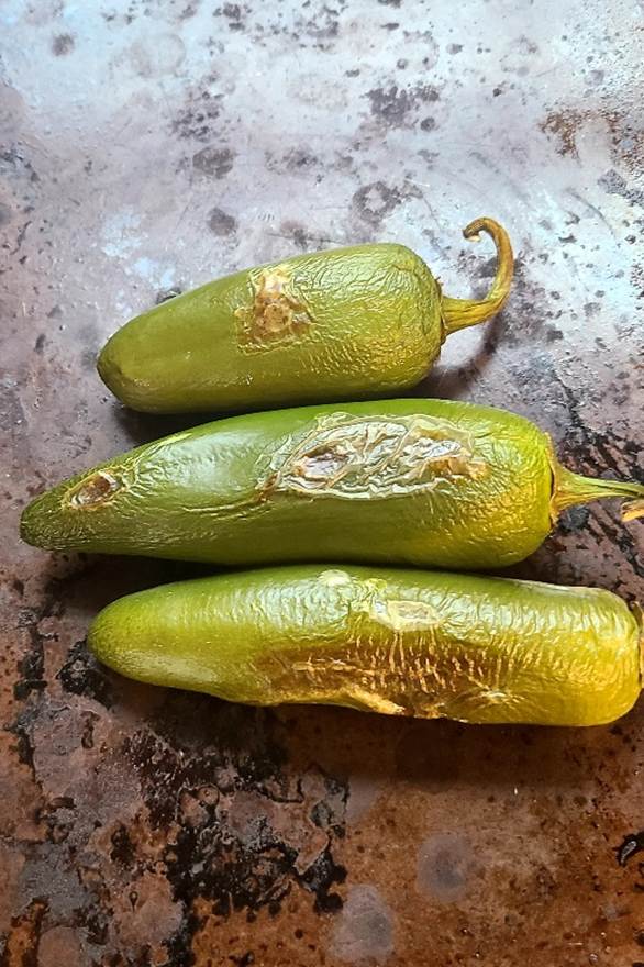 Three green roasted jalapeno peppers sitting on a baking sheet
